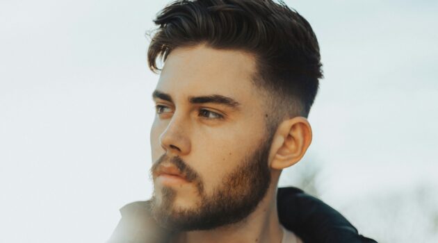Uomo in piedi all'aperto con capelli scuri e un taglio taper fade con la parte superiore strutturata