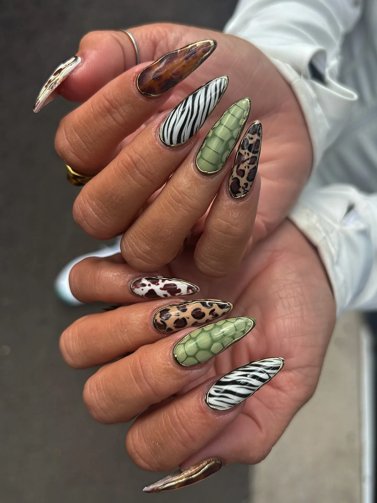 Unghie lunghe a mandorla con stampe tartaruga, zebra, leopardo e coccodrillo verde, impreziosite d'oro.
