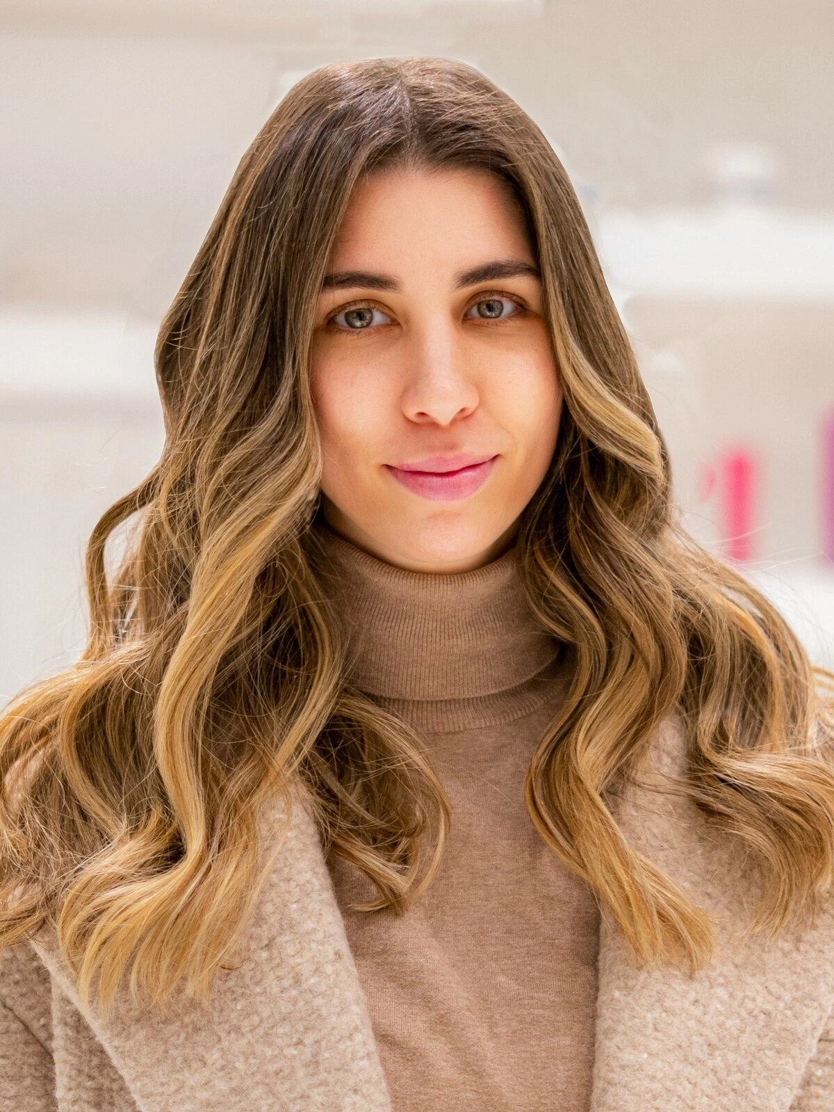 Una donna con un dolcevita e un cappotto di lana color cammello, con un balayage morbido e mosso in cui il castano sfuma in tonalità caramello