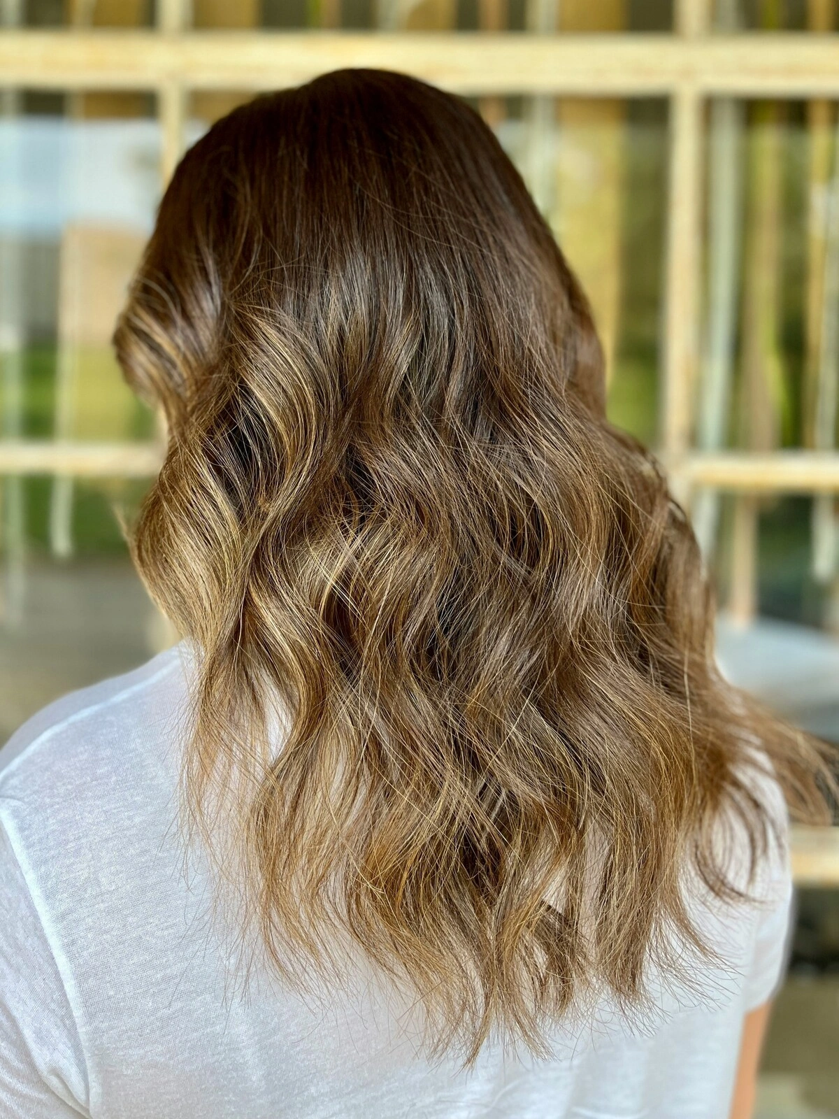 Veduta posteriore della testa di una donna con capelli mossi con il balayage, in cui il colore scuro sfuma in tonalità calde