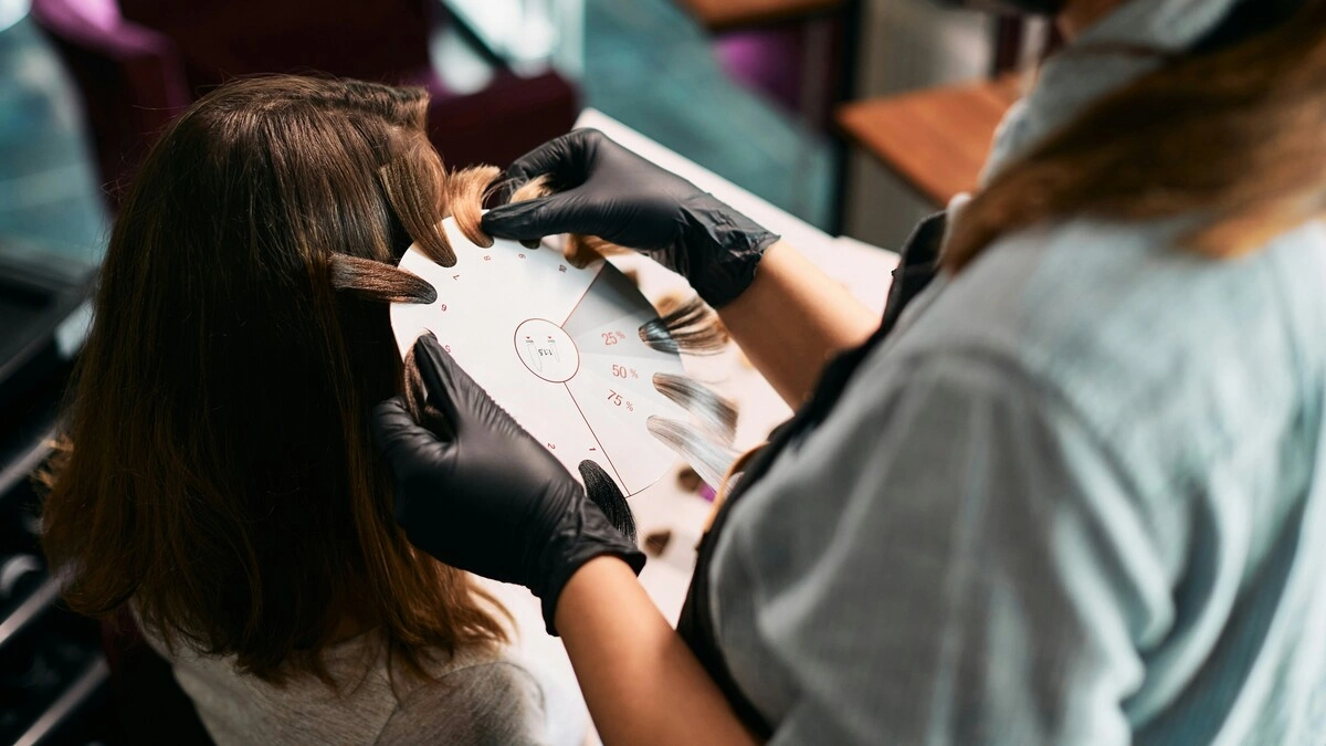 Primo piano di una colorista che accosta dei campioni di ciocche alla testa di una cliente per scegliere le tonalità del balayage