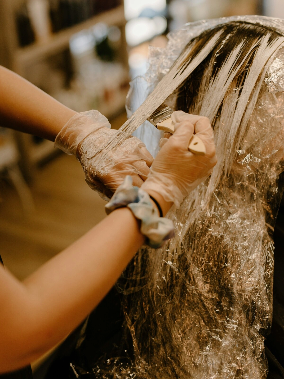 Una colorista con i guanti applica il colore con un pennello sui capelli di una cliente, durante un balayage