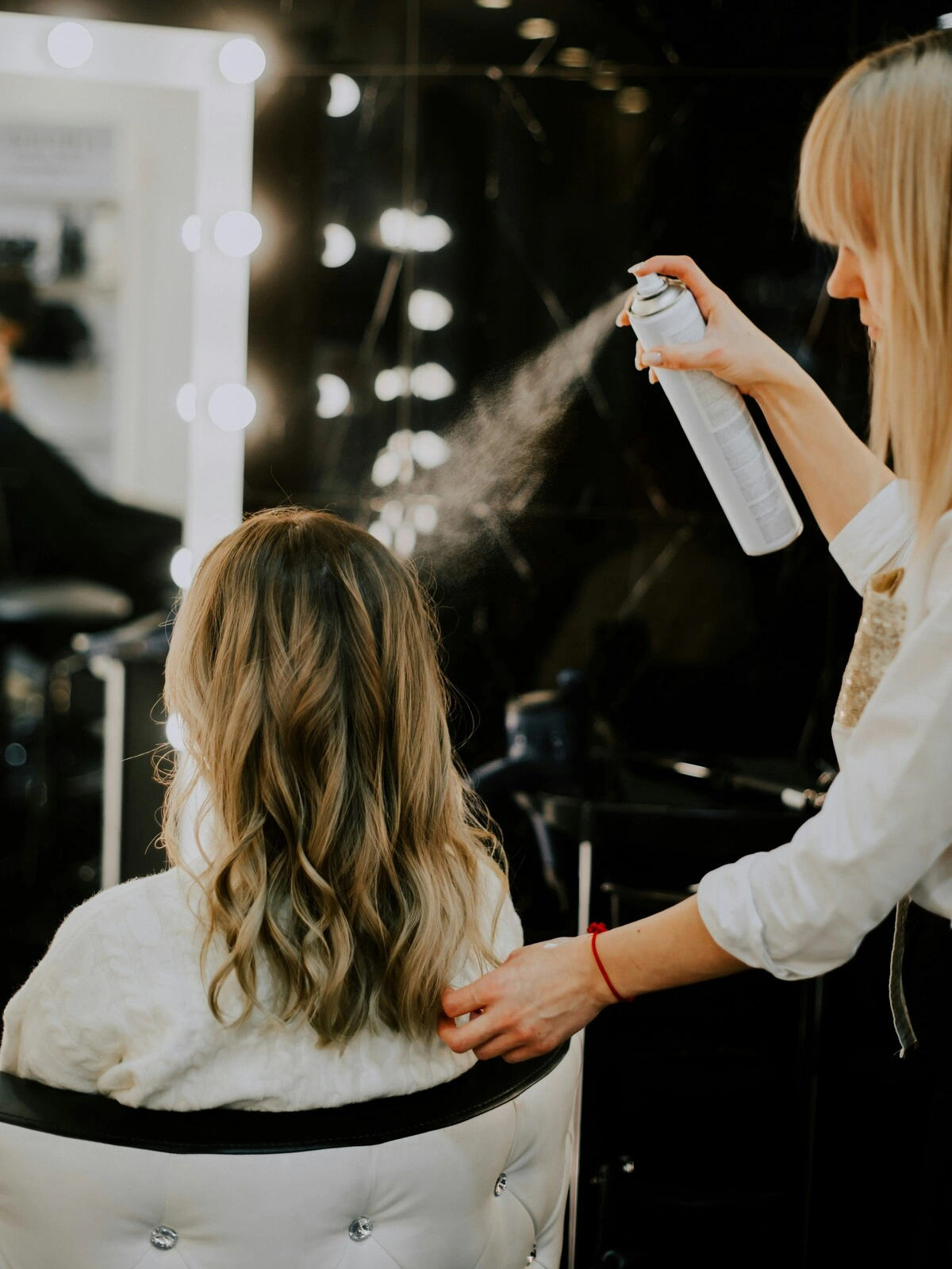 Una parrucchiera spruzza un prodotto di finitura sui capelli di una cliente dopo un balayage, la piega e lo styling a onde