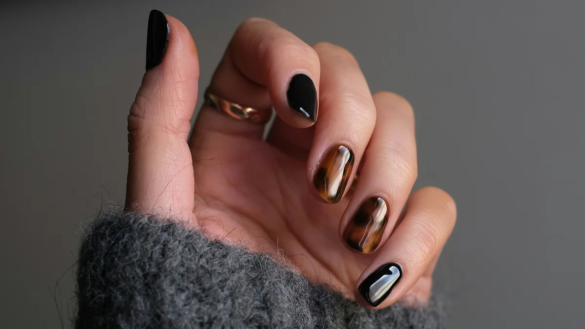 Primo piano di una mano con unghie corte e una manicure in gel lucida nelle tonalità nero e animalier