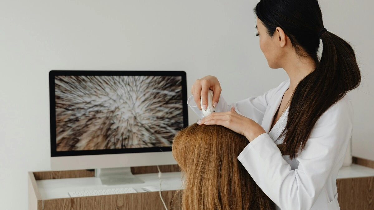 Una professionista osserva il cuoio capelluto di una cliente con una telecamera ad alta risoluzione e mostra l'immagine su un grande schermo