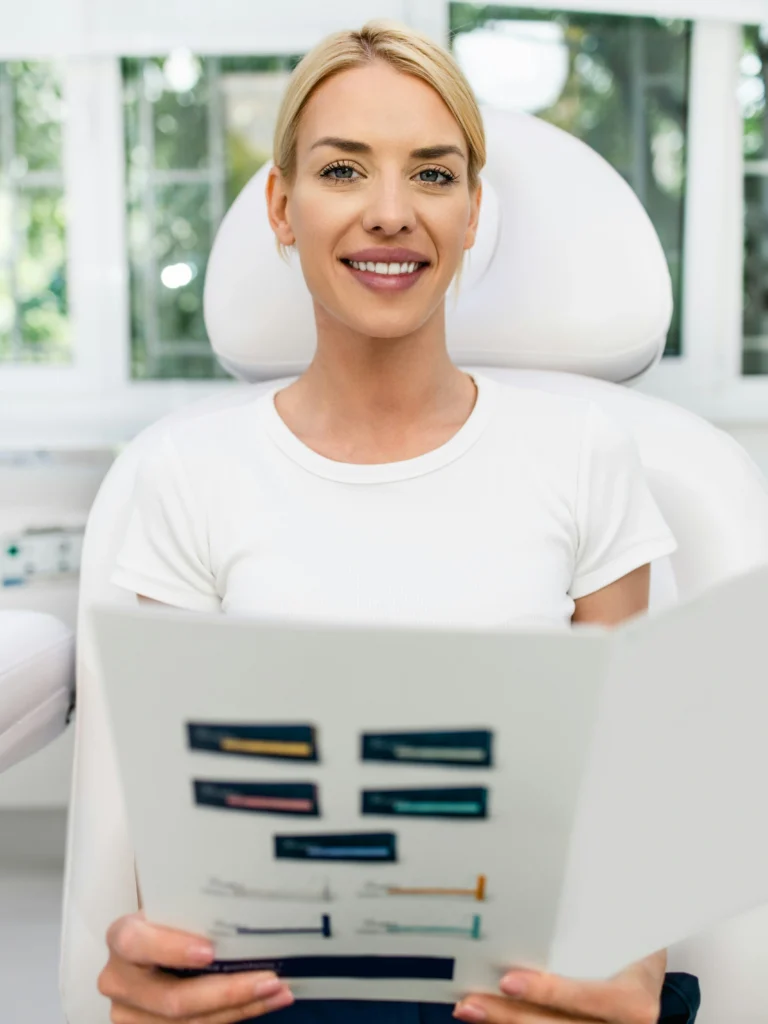 Una cliente è seduta in una clinica luminosa e pulita, sorride mentre tiene in mano un opuscolo informativo sui trattamenti viso