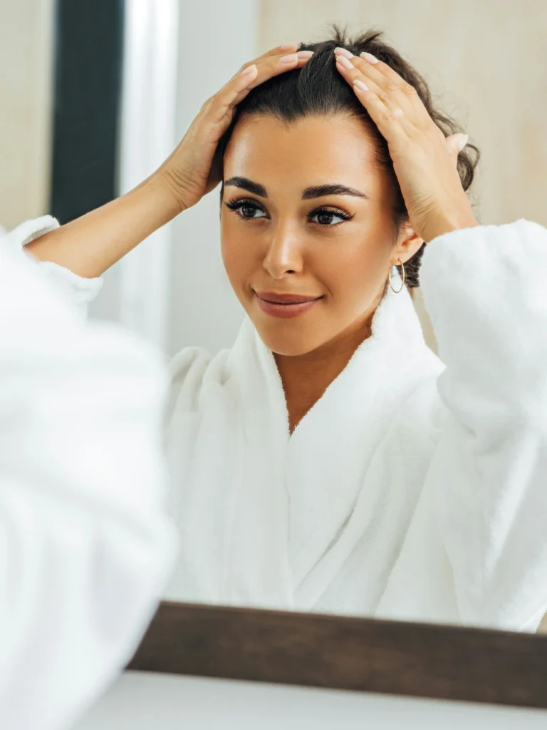 Una donna si scosta i capelli dal viso e sorride guardandosi allo specchio