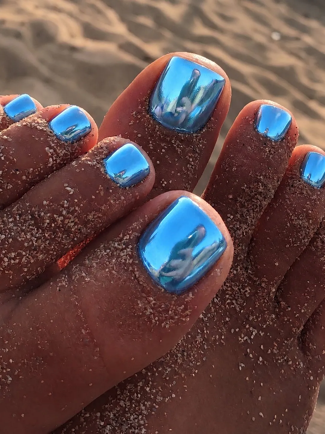 Pedicure cromata blu oceano metallizzata su piedi nella sabbia, in spiaggia