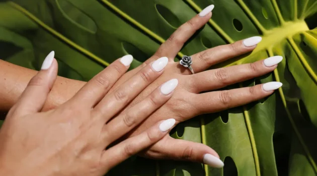 Foto in studio di unghie acriliche color nude appena fatte, forma a mandorla, su uno sfondo di foglie di palma