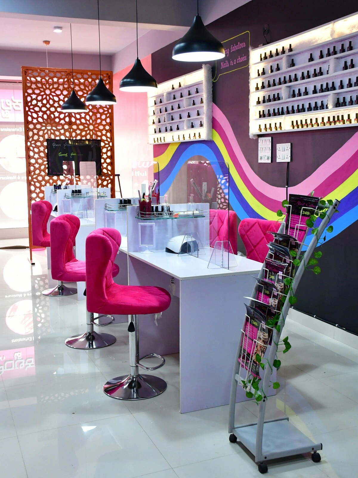 Interno di un centro unghie con postazioni bianche pulite e in ordine, poltroncine in velluto rosa e una parete viola