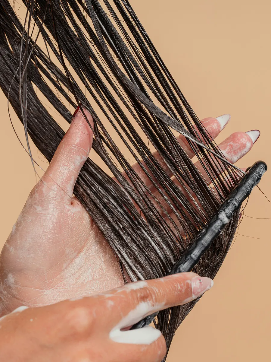 Primo piano di una donna che distribuisce il balsamo sui lunghi capelli con un pettine a denti larghi