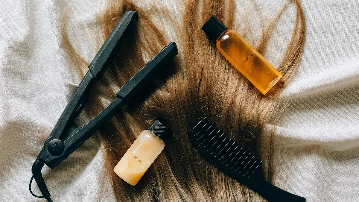 Flat lay di prodotti per la cura dei capelli disposti su una lunga chioma liscia, tra cui shampoo, balsamo, piastra e pettine a denti larghi
