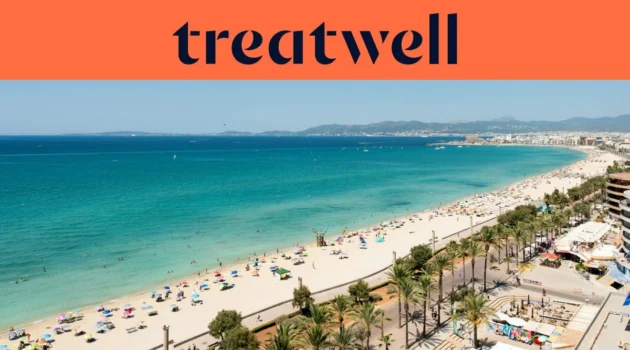 Veduta aerea di Playa de Palma a Maiorca, con una lunga distesa di sabbia dorata, file di ombrelloni, acqua turchese e calma e un lungomare costeggiato di palme che corre lungo la città, con le colline in lontananza sotto un cielo azzurro e limpido.