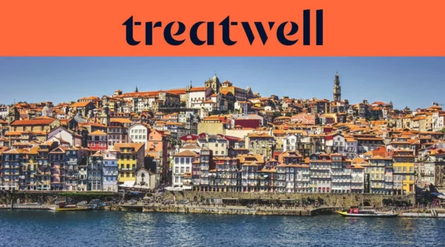 Il lungofiume della Ribeira a Porto, con le sue file di case colorate e tetti in cotto che si arrampicano sulla collina dal fiume Douro, e la torre dei Clérigos sullo skyline sotto un cielo azzurro limpido.