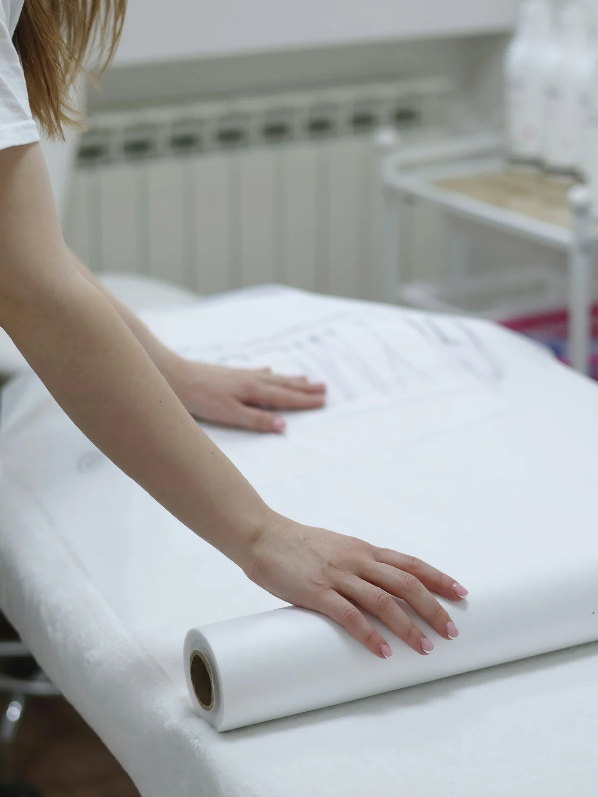 Primo piano delle braccia di un'estetista che srotola un foglio di carta pulita su un lettino per preparare un trattamento