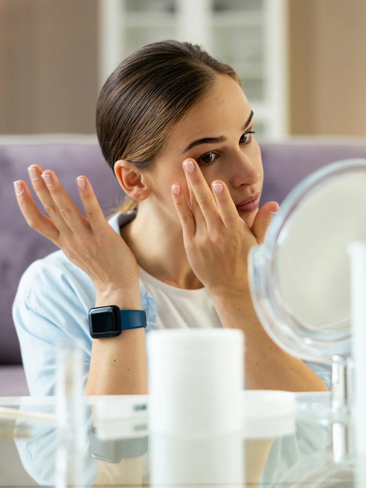 Una donna seduta a un tavolo applica con delicatezza crema idratante e oli sul viso e sulle sopracciglia