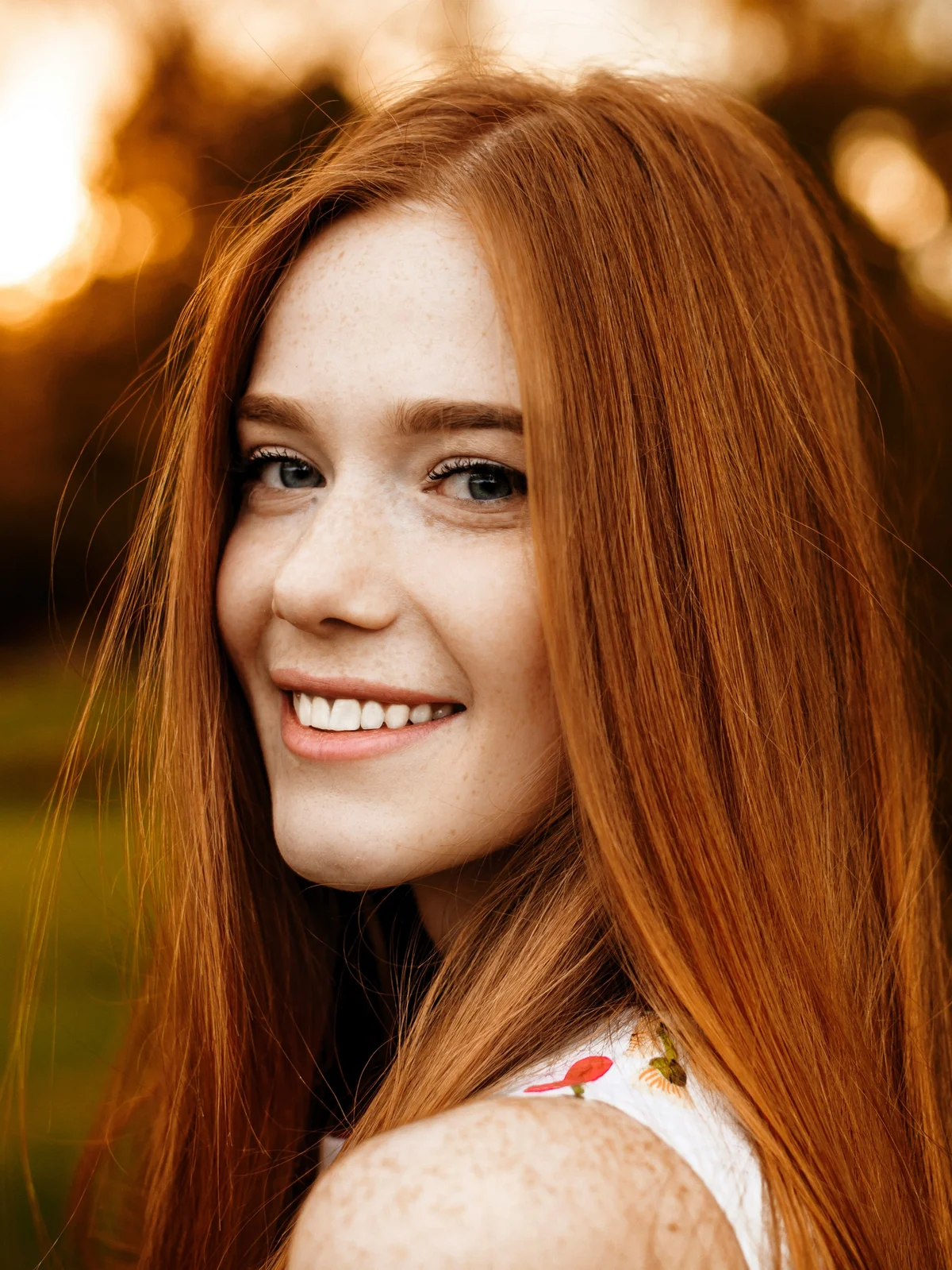 Una donna con lunghi capelli rossi e sopracciglia ordinate e definite sorride mentre passeggia all'aperto nella natura, nella luce calante del giorno