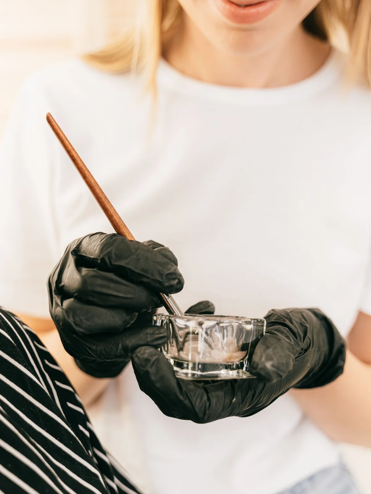 Primo piano di un'estetista che tiene un piccolo vasetto di vetro e un pennellino sottile mentre mescola la tinta per sopracciglia in salone