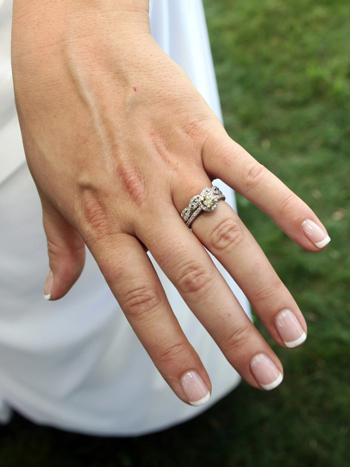 La mano di una donna con una curata French manicure in una combinazione classica di nude e bianco su unghie corte dalla forma squadrata-ovale