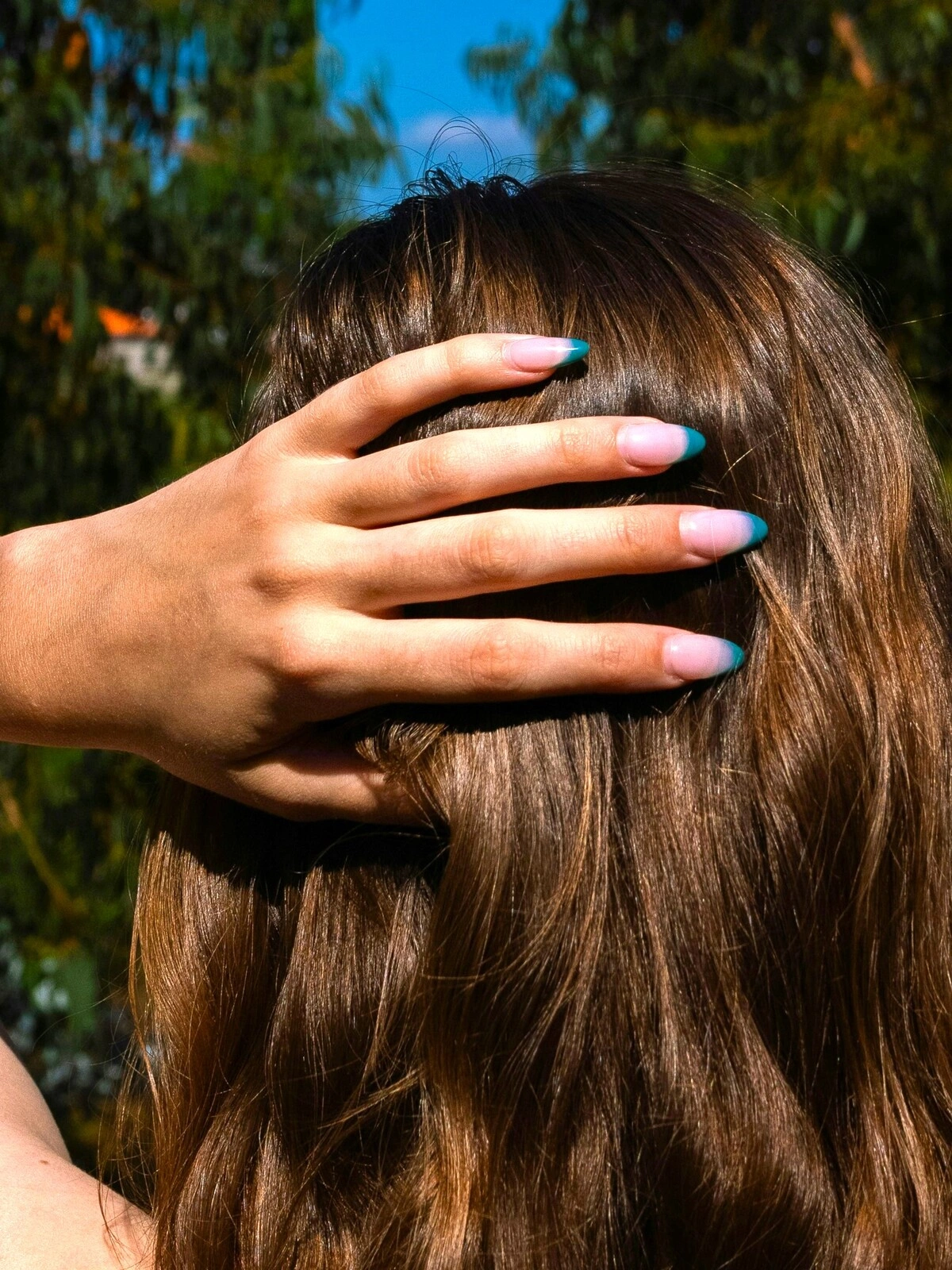 La mano di una donna appoggiata dietro la nuca mostra una French manicure dalla base rosa chiaro e punte verde acqua su unghie a mandorla