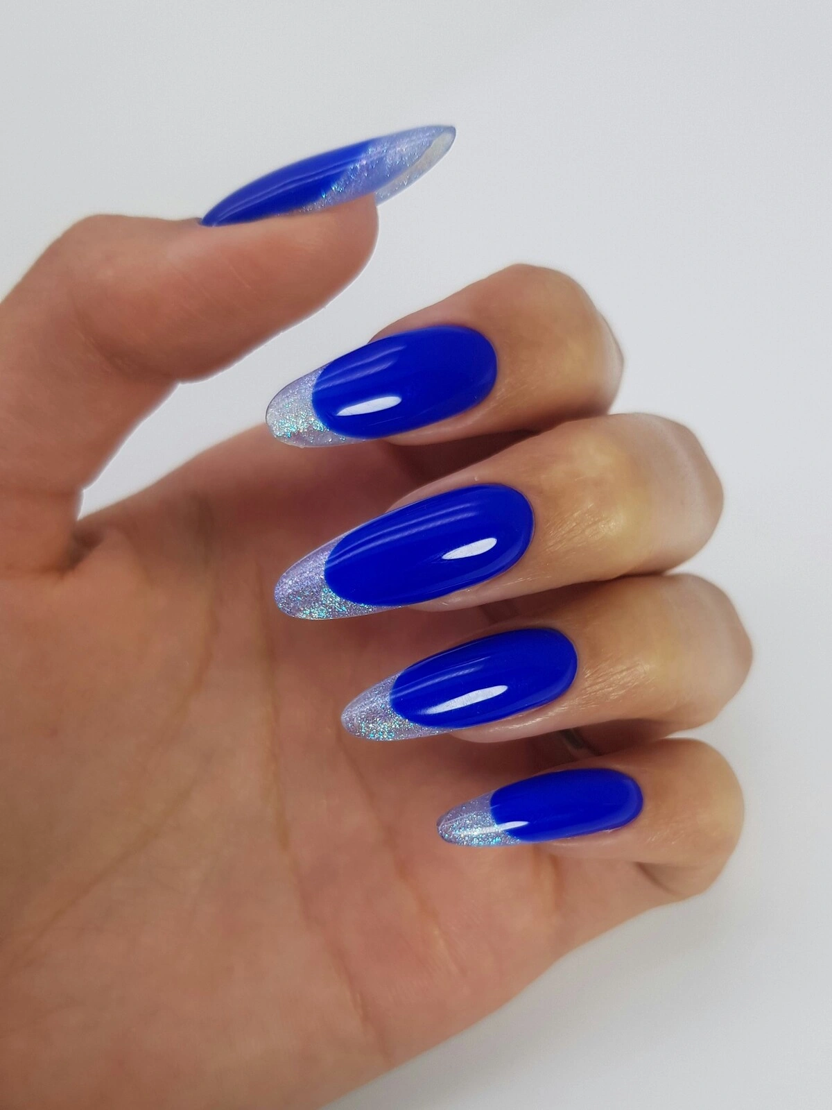 La mano di una donna con un'audace French manicure dalla base blu acceso e punte metallizzate argento su unghie lunghe a mandorla