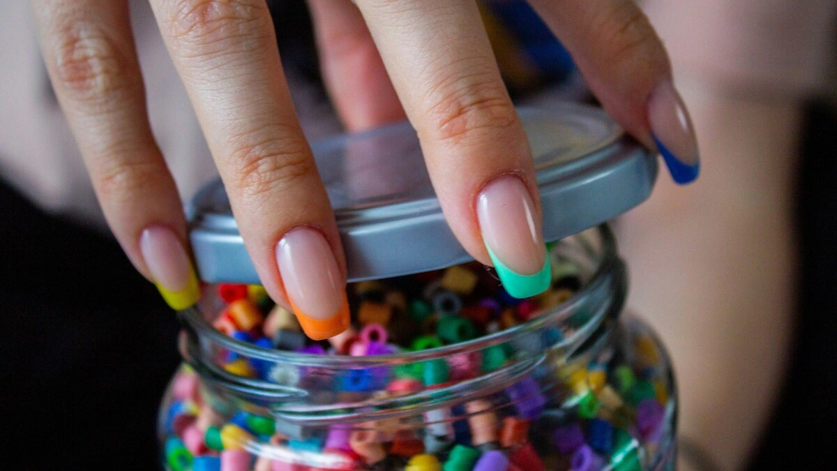 La mano di una donna con una French manicure con base nude trasparente e punte multicolori