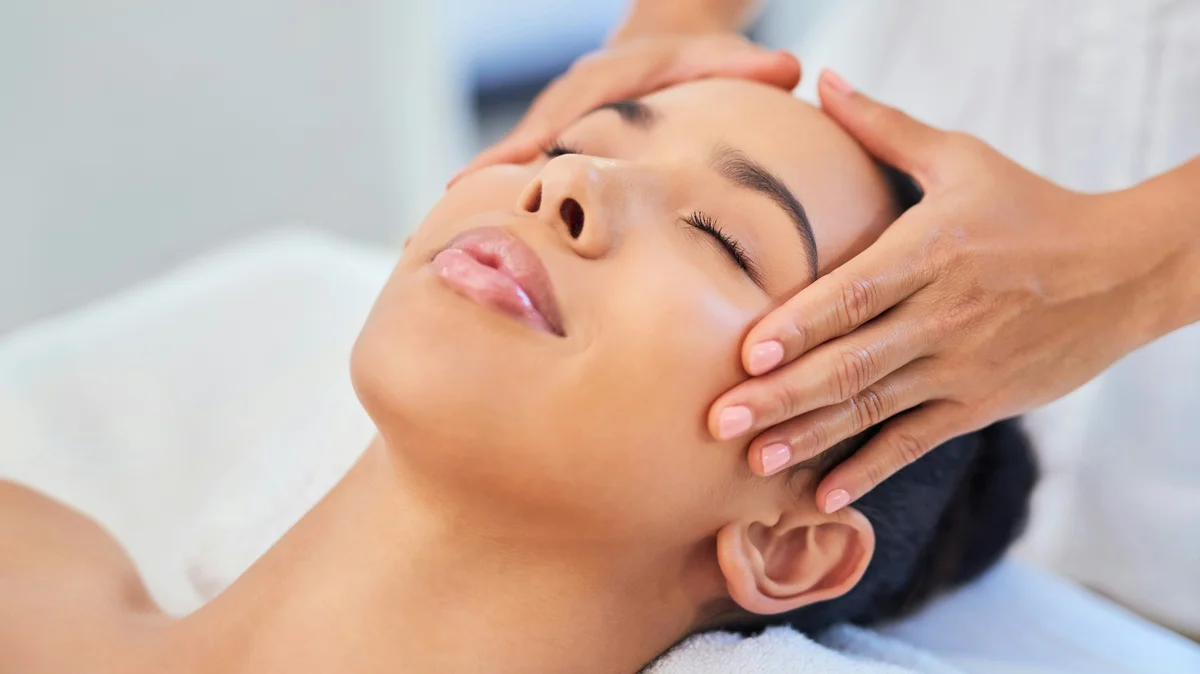 Una donna distesa in un centro estetico mentre un'estetista le appoggia delicatamente le mani sulla testa durante un trattamento viso