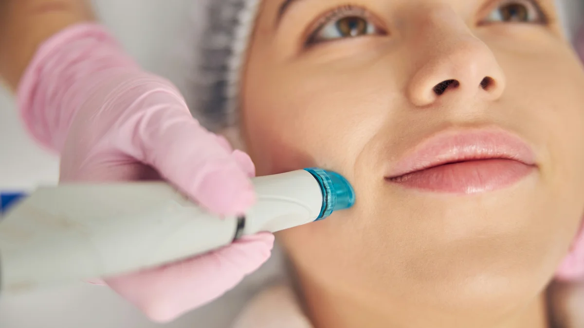 Primo piano di un dispositivo HydraFacial che scivola sulla guancia di una cliente durante un trattamento in salone