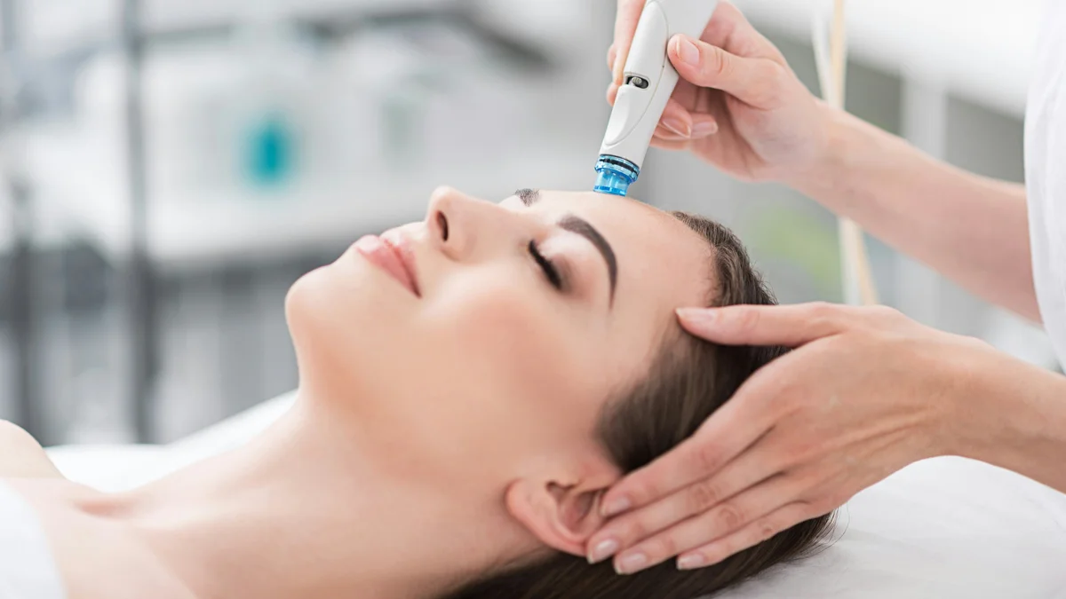 Primo piano di una donna rilassata con gli occhi chiusi durante un trattamento HydraFacial in un salone tranquillo