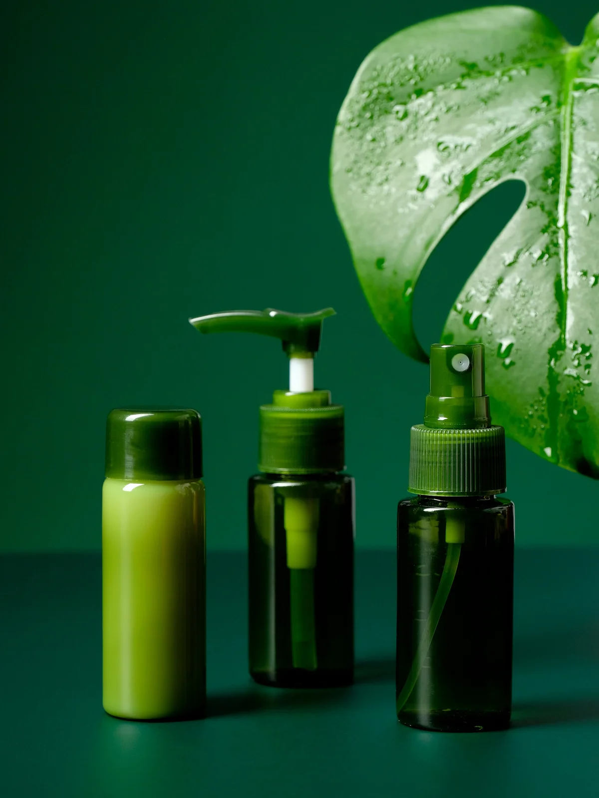 Foto prodotto di tre gel e creme lenitivi in flaconi verdi, con una grande foglia tropicale verde sullo sfondo