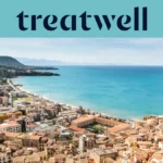 Ampia veduta su una cittadina costiera siciliana, con edifici antichi dai tetti in cotto, una mezzaluna di spiaggia sabbiosa, mare turchese cristallino e un promontorio roccioso che si erge su un lato.