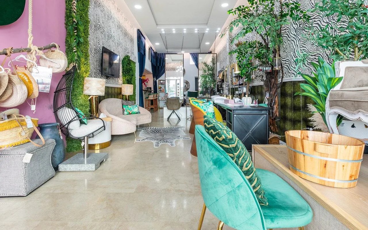 L'interno di Brazilian Beauty Marbella, un salone luminoso con pareti a stampa zebrata, una parete di piante vere, poltrone in velluto turchese e una bacinella per pedicure in legno.