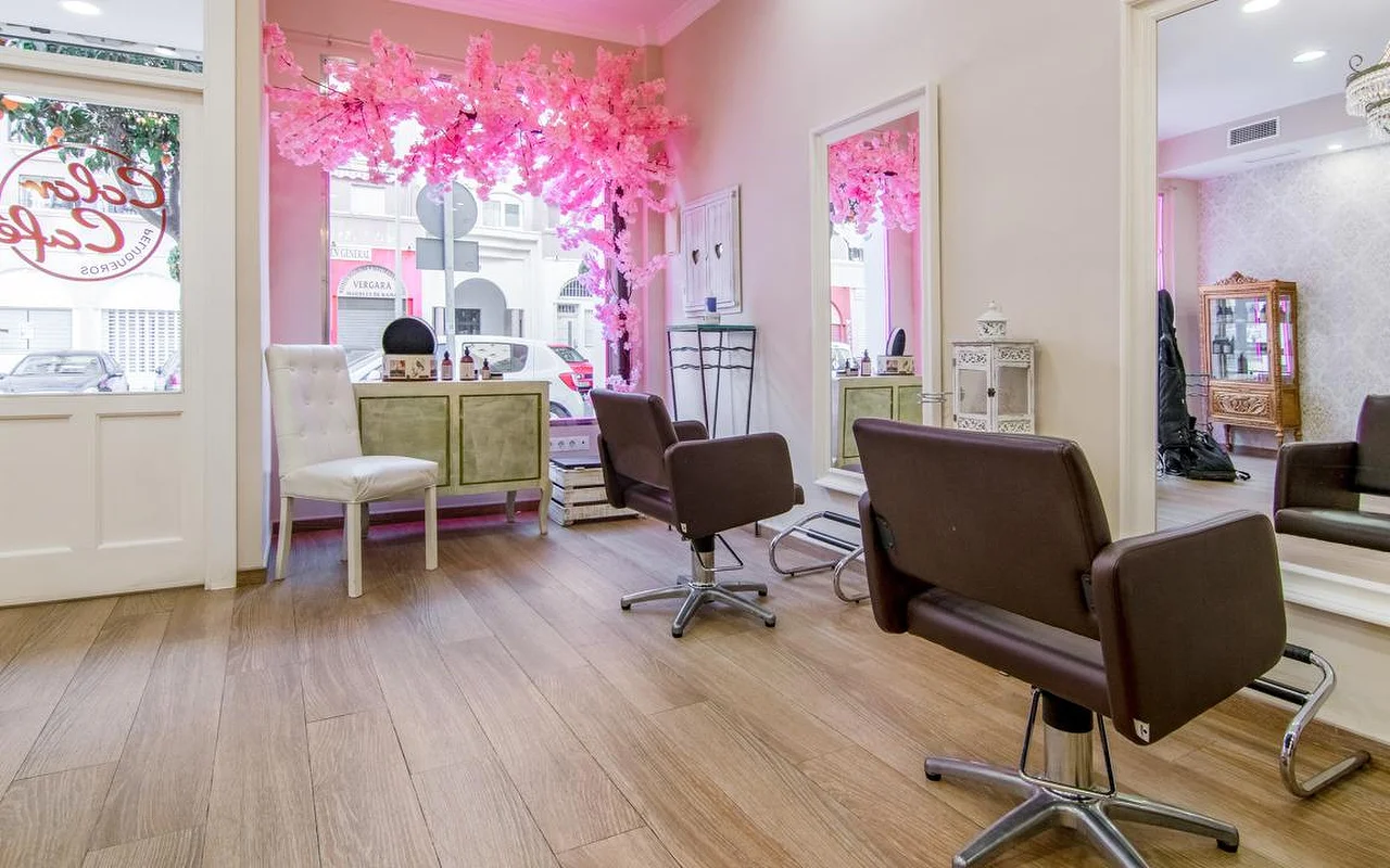L'interno di Color Café Peluqueros a Torremolinos, un salone con pareti rosa, poltrone marroni, grandi specchi e una composizione di ciliegio in fiore rosa in vetrina.