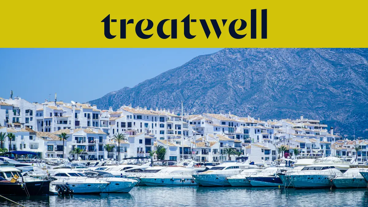 Il porto turistico di Puerto Banús, a Marbella, circondato da edifici bianchi e yacht ormeggiati sullo sfondo delle montagne, sotto uno striscione giallo Treatwell.