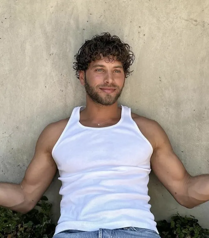 Taglio riccio dall'effetto naturale e voluminoso su capelli castano scuro, ritratto estivo rilassato