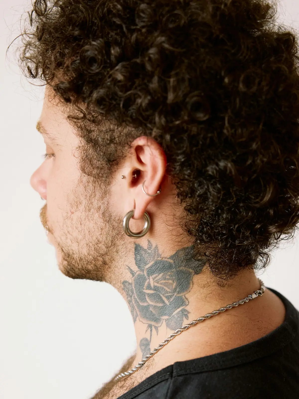 Foto da dietro di un uomo con piercing al lobo, all’helix e al tragus