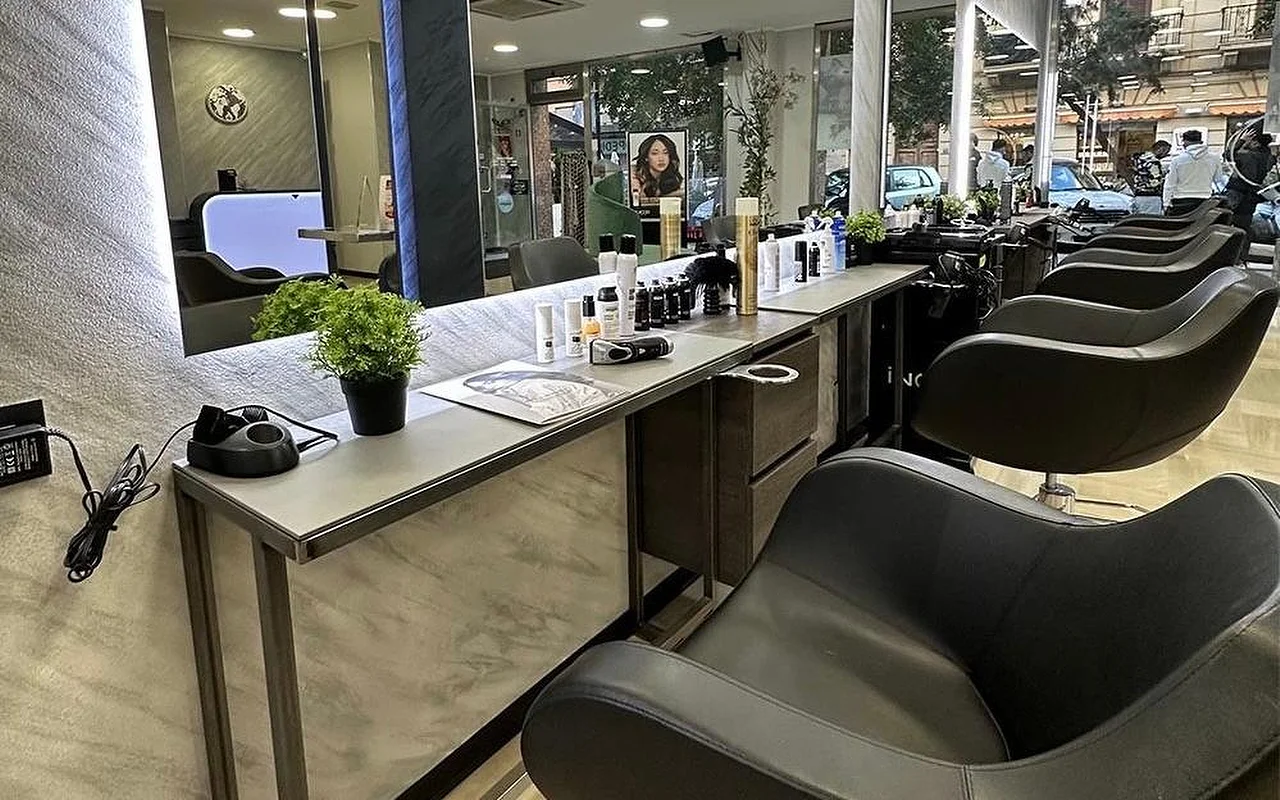 L'area styling di Equipe Beauty, con una fila di poltrone nere lungo un bancone effetto marmo, un grande specchio retroilluminato, prodotti per lo styling e una pianta in vaso sul bancone, e vetrate dal pavimento al soffitto che affacciano sulla strada.