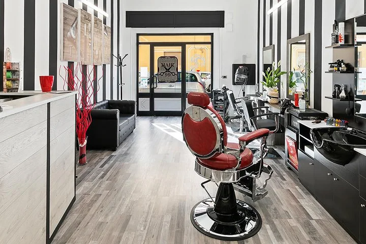 Poltrona da barbiere vintage rossa da Hair 99 ad Alghero, con le caratteristiche pareti a righe bianche e nere.