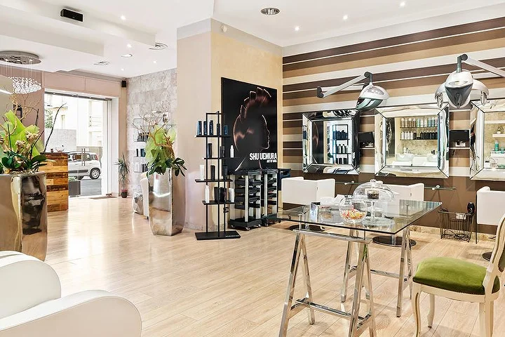 Postazioni di styling eleganti al salone Hair Queen di Cagliari con pareti a righe crema e marroni e alti vasi argentati.