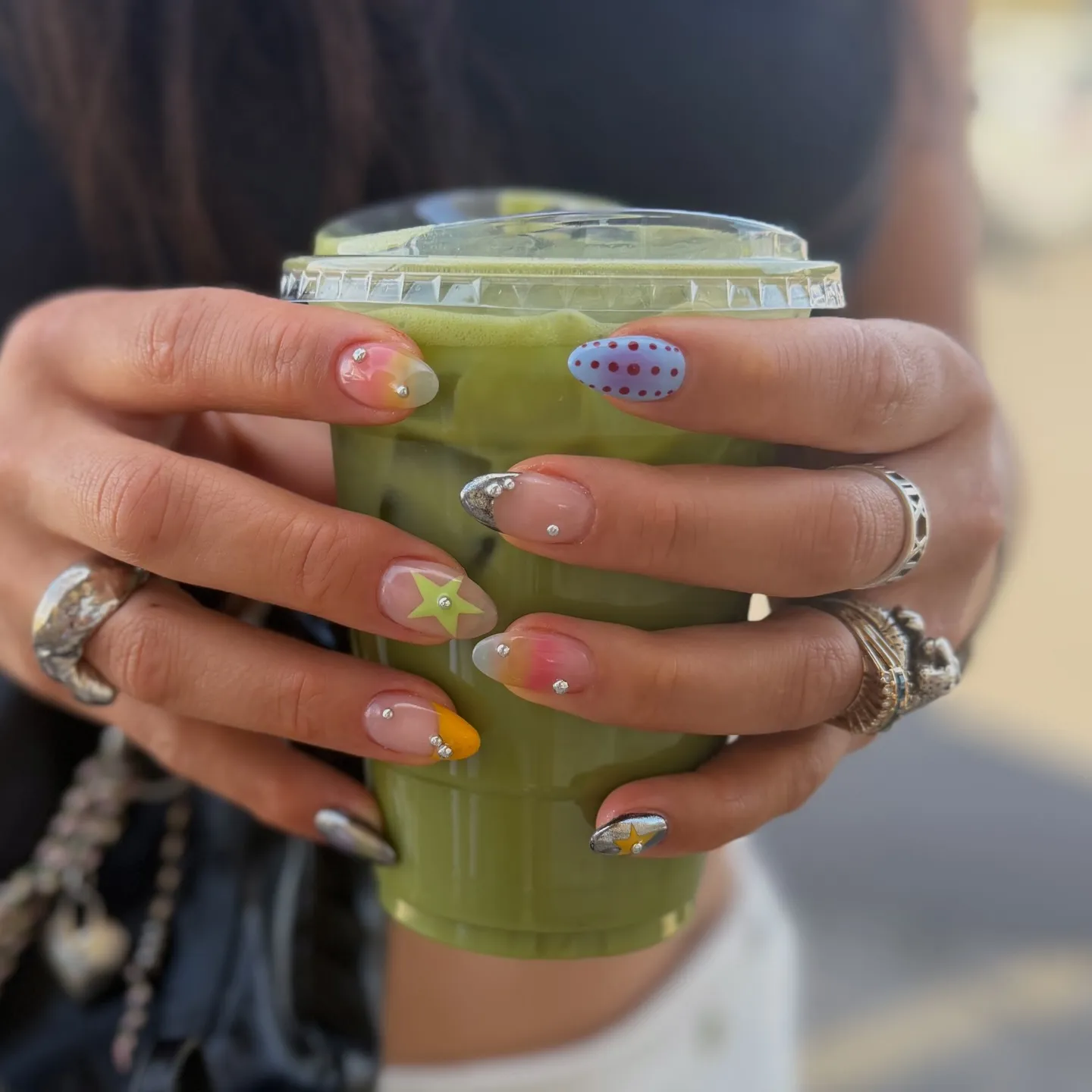 Set di nail art assortita con piccoli piercing di cristallo, motivi a stella e accenti colorati su unghie a mandorla