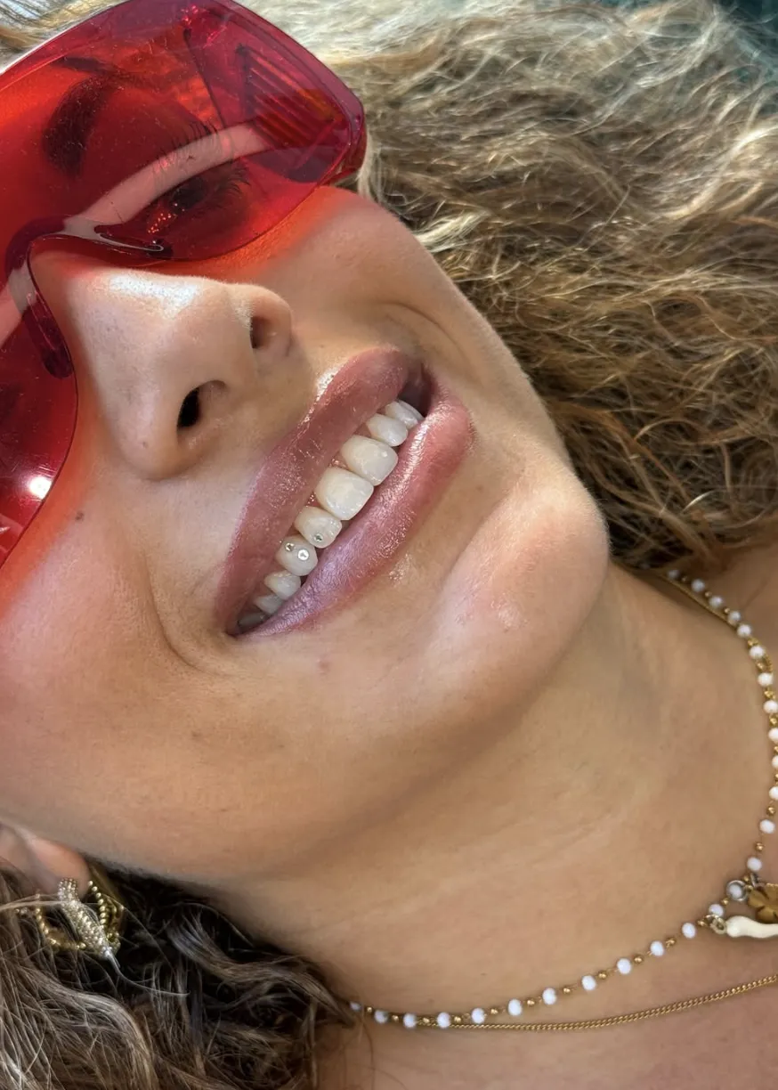 Primo piano di un sorriso con due piccoli brillantini di cristallo sui denti inferiori, ritratto estivo