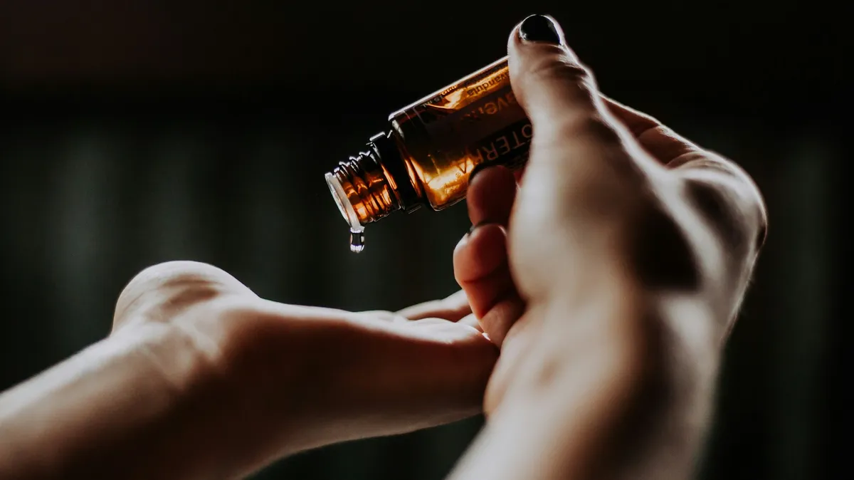 Primo piano delle mani di una professionista che con una mano versa alcune gocce di olio da una bottiglietta di vetro nel palmo dell'altra