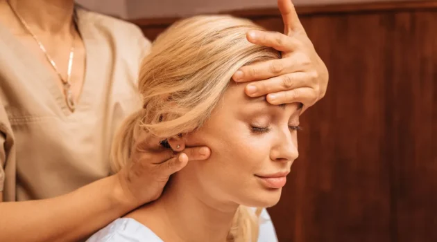 Primo piano di una donna con gli occhi chiusi mentre una professionista, durante un massaggio indiano della testa, le appoggia una mano sulla fronte e con l'altra le massaggia il collo